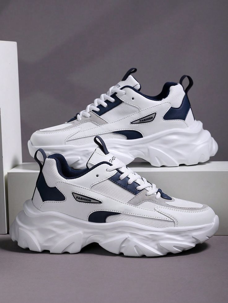 White chunky sneakers with navy blue accents, breathable mesh panels, lace-up closure, and a thick sculpted sole for a stylish streetwear look.
