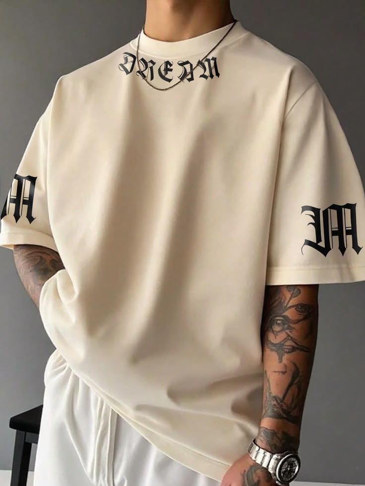 Men's oversized cream white T-shirt featuring black Gothic-style "DREAM" lettering on the collar and matching graphic prints on both sleeves for a modern streetwear look.